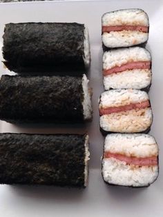 four sushi rolls on a white plate with rice and ham in the middle one is cut in half