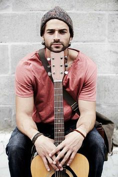 a man with a guitar sitting in front of a brick wall