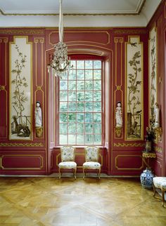 an ornate room with red walls and paintings on the wall, two chairs in front of a window