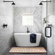 a white bath tub sitting under a window next to a wooden mat on the floor