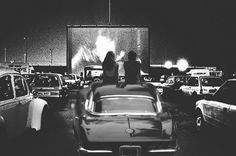 two people sitting on top of a car in front of a movie screen