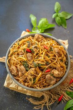 a bowl filled with noodles and meat on top of a cloth next to basil leaves