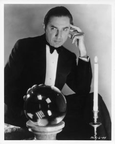 a man in a tuxedo sitting at a table with a glass ball and candle