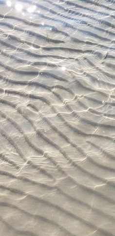 some sand and water on a beach with sun shining through the clouds in the background