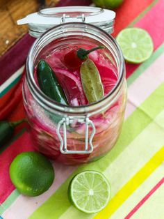 a mason jar filled with pickles and limes on a colorful table cloth next to sliced limes