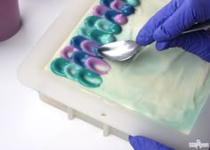 a person in purple gloves is decorating a cake with white frosting and blue icing