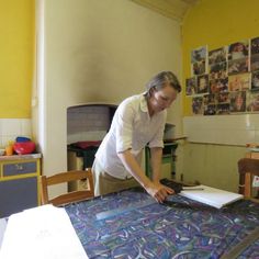 a woman in white shirt cutting paper on top of a blue and purple table cloth