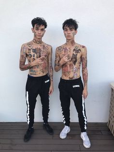 two young men with tattoos standing next to each other in front of a white wall