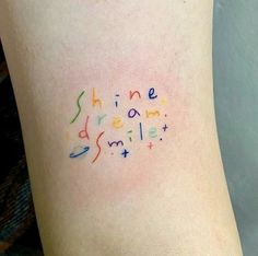 the word shine dream smile written in multicolored letters on the back of a woman's leg