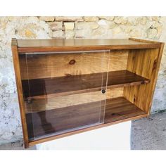 a wooden cabinet with glass doors on the front and bottom shelves, against a stone wall