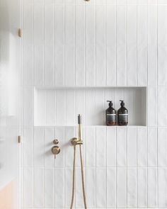 a white tiled bathroom with gold fixtures and shower faucet in the corner next to it