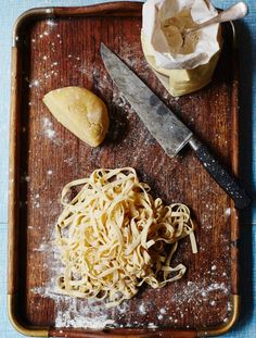 a wooden cutting board topped with pasta next to a knife