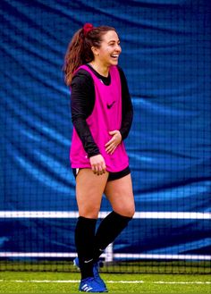 a woman in pink shirt and black shorts standing on grass next to soccer goal net