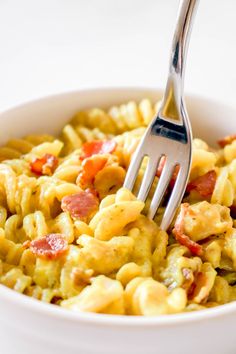 a fork in a bowl filled with macaroni and cheese, topped with bacon