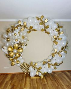 a wreath made out of balloons and gold leaves on a wooden floor in front of a white wall