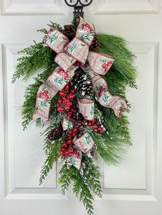 a christmas wreath hanging on a door with pine cones and evergreen leaves, red berries, and bells