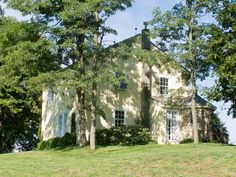 a large white house sitting on top of a lush green hillside next to trees and grass