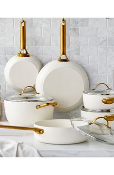 white pots and pans with gold handles sit on a marble countertop in front of a brick wall