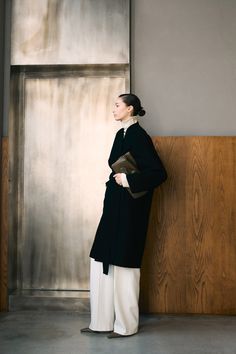 a woman standing in front of a wall with her hands on her hips and looking off to the side