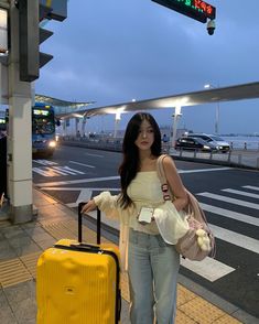 a woman standing next to a yellow suitcase at an airport with her hand on the handle