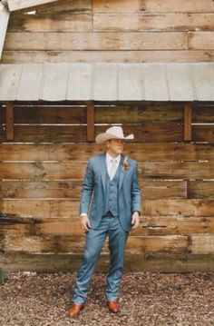 a man in a blue suit and hat standing next to a wooden building with a metal roof