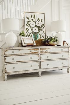 a white dresser with two vases on top of it next to a stair case