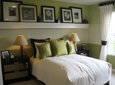 a bedroom with green walls and pictures on the wall above the bed, along with two lamps