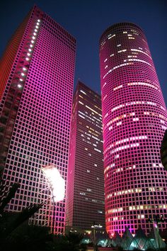 two tall buildings lit up at night with pink lights in the windows and one building has an apple logo on it