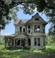 an old abandoned house sitting in the middle of a field with trees and grass around it