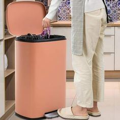 a person standing next to a trash can in a kitchen with tile walls and flooring