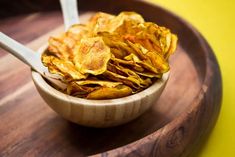 a wooden bowl filled with potato chips on top of a table next to a spoon