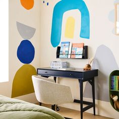 a bedroom with a desk and chair next to a wall painted with colorful shapes on it