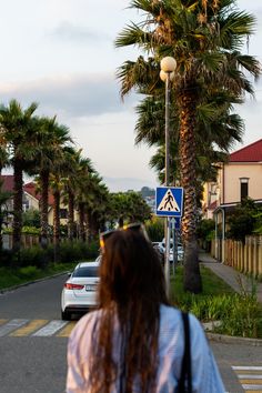 a woman is walking down the street in front of palm trees and a blue sign