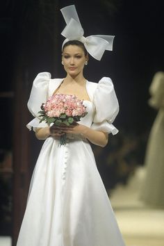 a model walks down the runway wearing a wedding dress and holding a bouquet of flowers