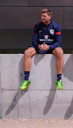 a man sitting on top of a cement wall next to another man wearing green shoes