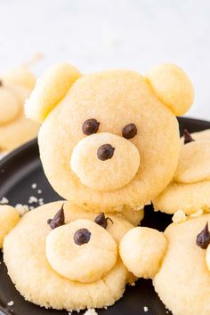 cookies shaped like teddy bears on a black plate with white sprinkles around them