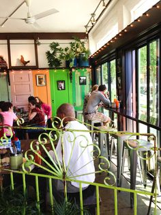 people sitting at tables in a restaurant with green walls and doors, surrounded by potted plants