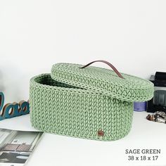 a green knitted basket sitting on top of a white table next to other items