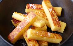 some french toast sticks are in a black bowl on a counter top, with sugar sprinkled on them