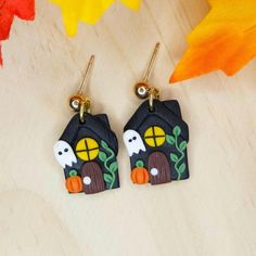 two small houses with pumpkins and leaves in front of them on a wooden surface