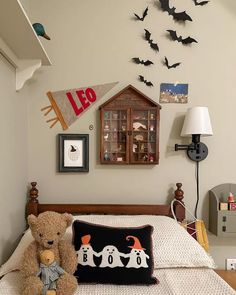 a teddy bear sitting on top of a bed next to a lamp and framed pictures