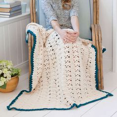 a woman sitting in a chair with a crocheted blanket on top of it