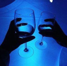 two people holding up wine glasses in front of a blue lit tablecloth with white and black designs on it