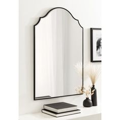 a mirror sitting on top of a white shelf next to a vase and book in front of it