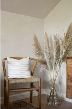 a wooden chair sitting next to a vase filled with dry grass on top of a hard wood floor