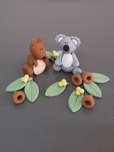 two toy animals sitting next to each other on top of a gray surface with leaves and flowers