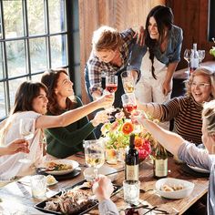 a group of people toasting wine glasses at a table with food and drinks on it