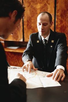 two men in suits are sitting at a table and one man is pointing to something