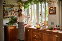 a woman standing in a kitchen preparing food on top of a counter next to a window