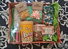 a box filled with lots of candy and candies on top of a bed next to a cup